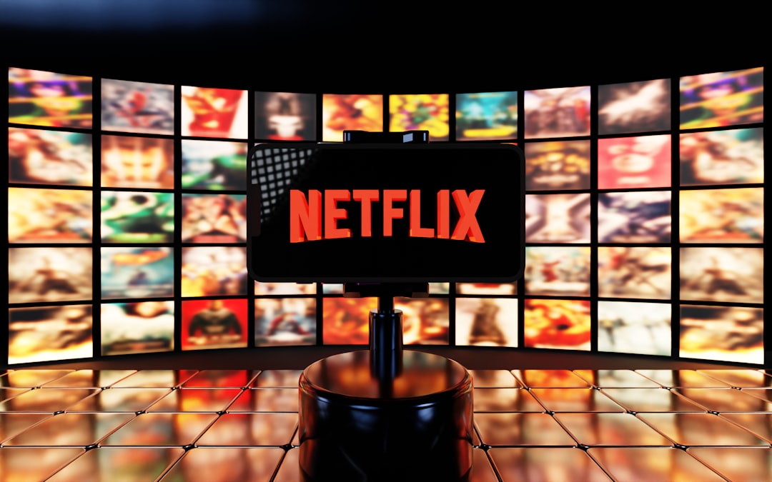 About A smartphone displays the Netflix logo in bright red, set against a background of vibrant, colorful movie thumbnails and a glossy tiled surface. The cinematic atmosphere highlights streaming culture and digital entertainment.